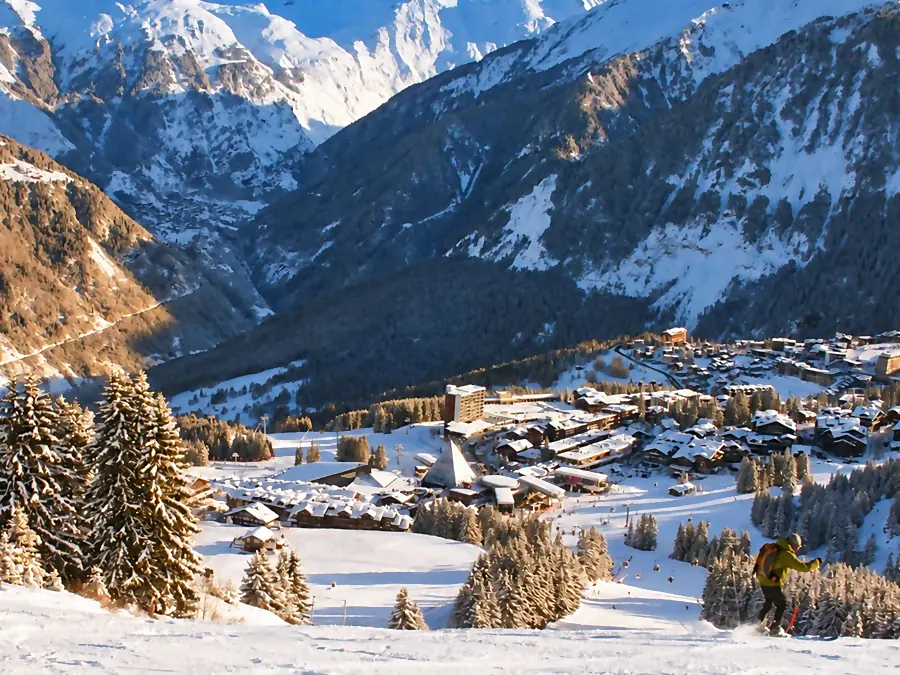 Un skieur sur une piste au-dessus de Courchevel 1850, ses chalets sous la neige et la vallée entre les sommets