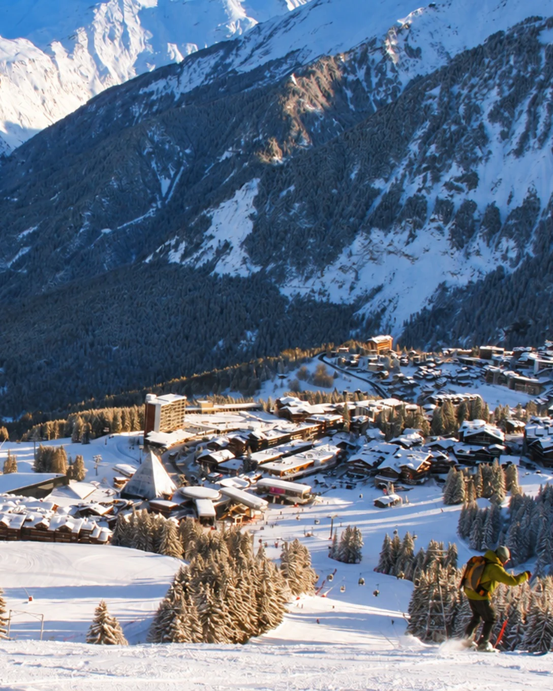 A skier on a run above Courchevel 1850, its snow-covered chalets and the valley between the peaks