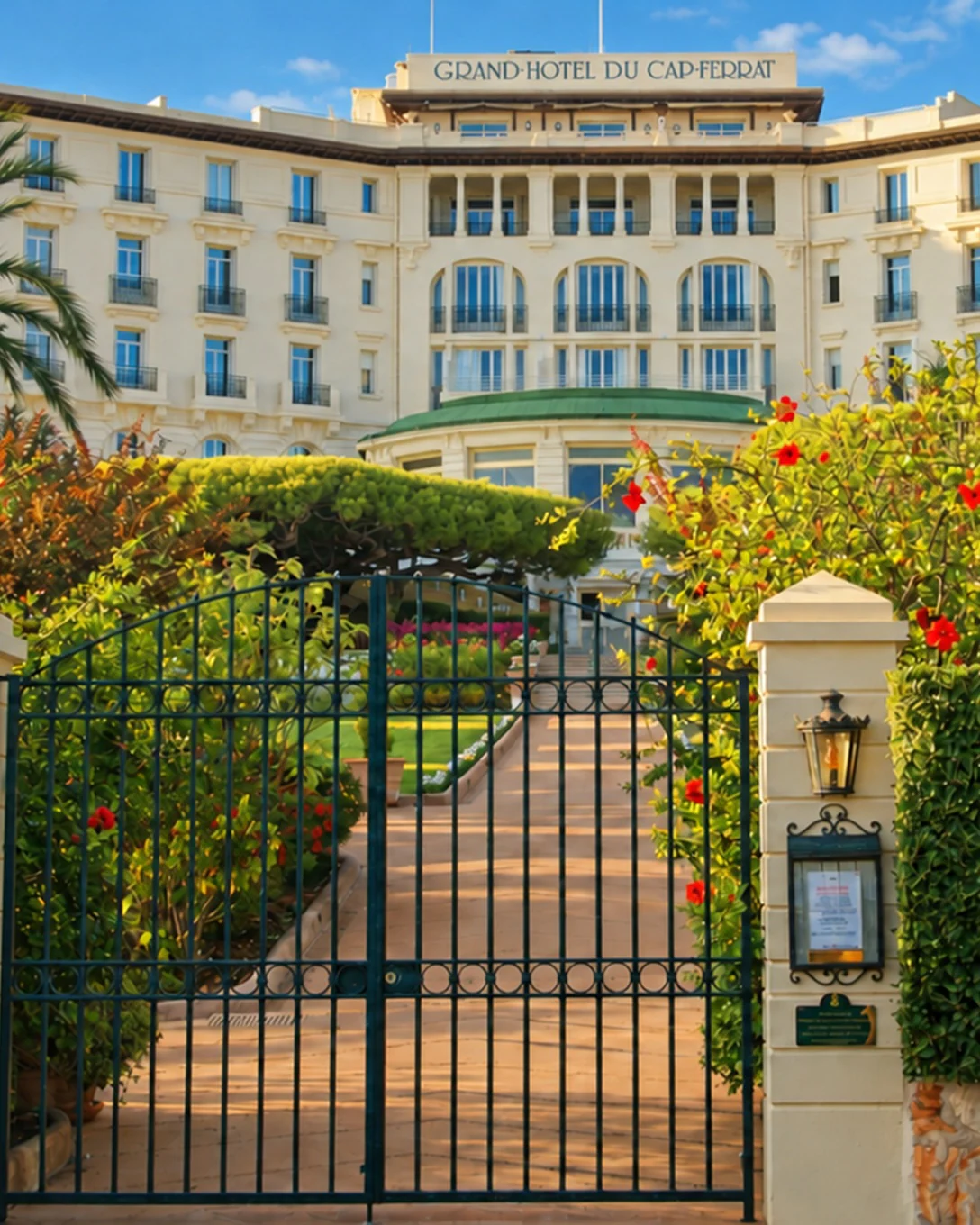 La façade du Grand-Hôtel du Cap-Ferrat au bout de son allée fleurie, entre pins et palmiers