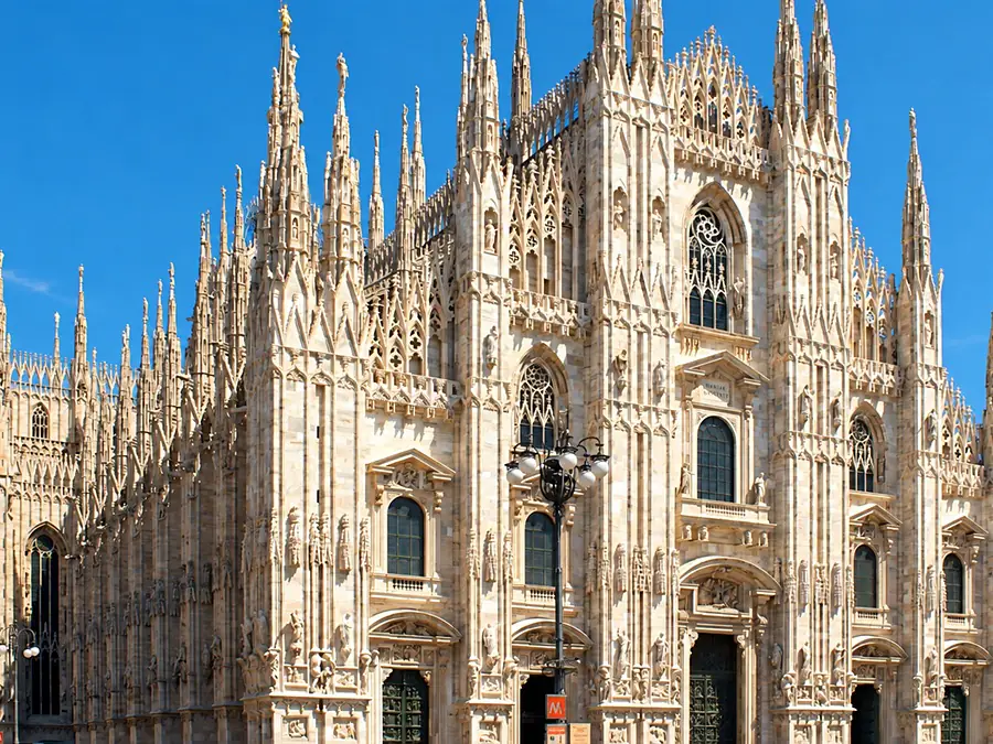 The marble facade of Milan Cathedral and its Gothic spires, under a blue sky