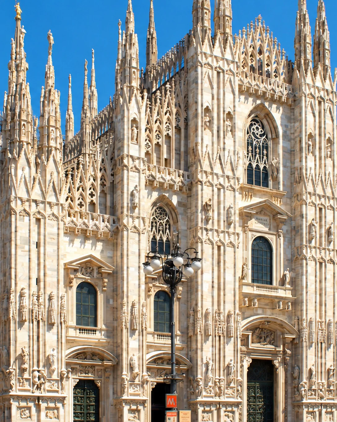The marble facade of Milan Cathedral and its Gothic spires, under a blue sky