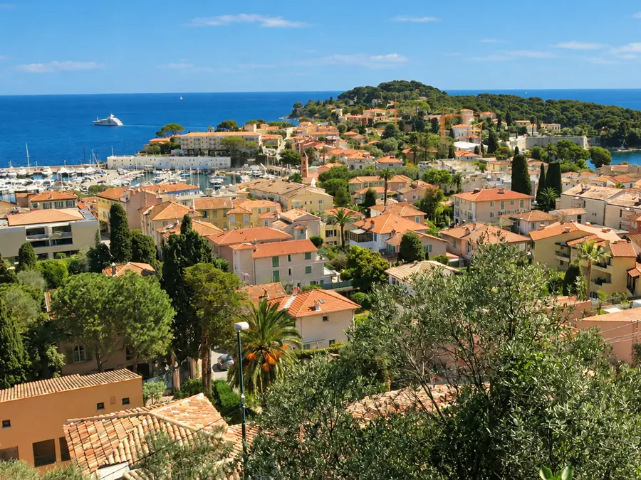 Le village de Saint-Jean-Cap-Ferrat, ses toits et son port, avec la pointe boisée de la presqu’île au loin