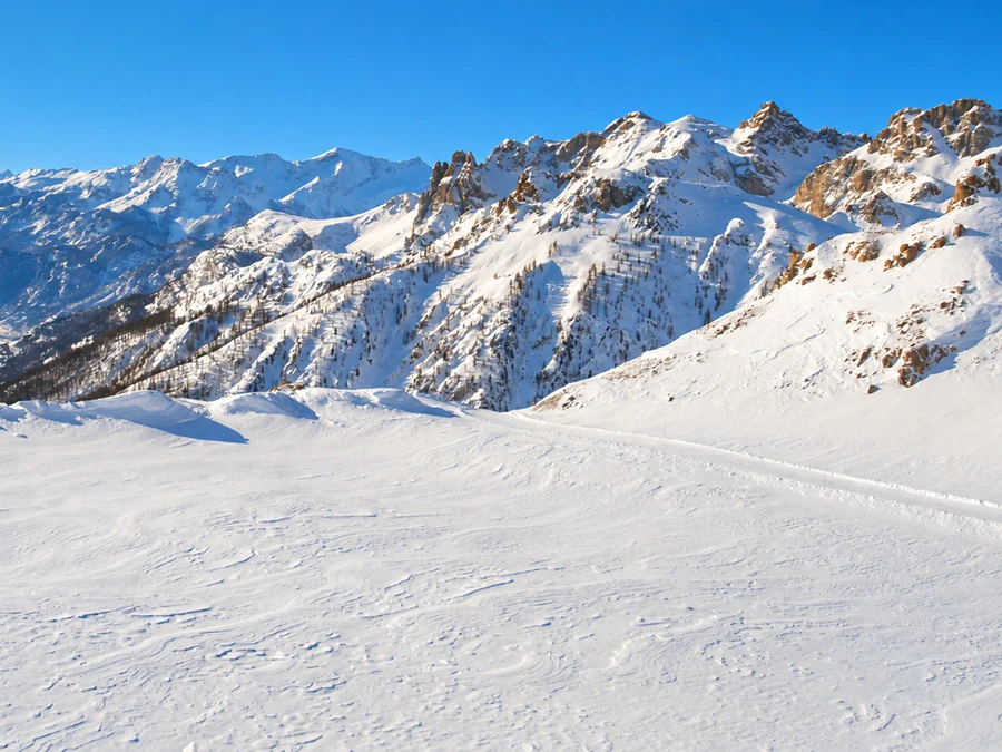 A wide snowfield below rocky peaks under a clear winter sky