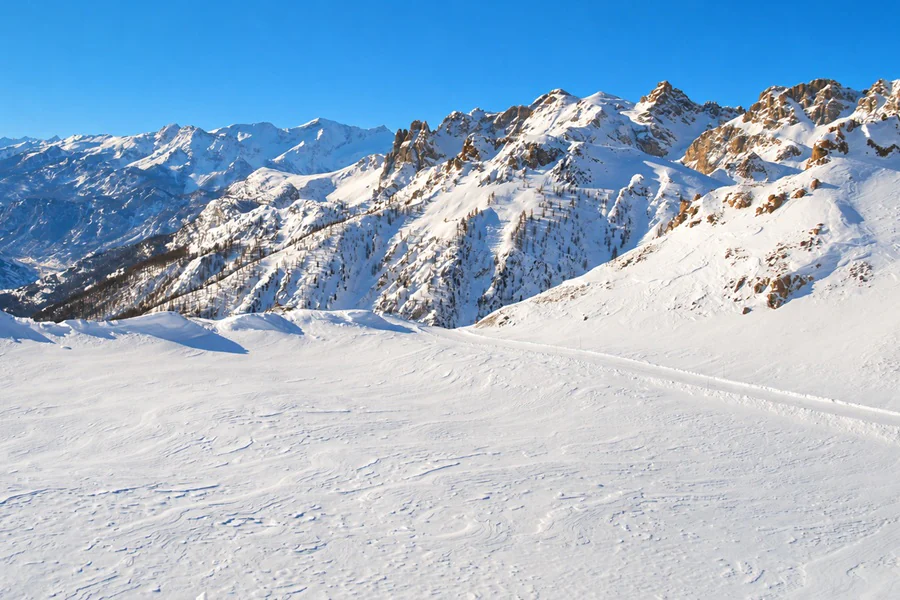 Un vaste plateau enneigé au pied de sommets rocheux, sous un ciel d’hiver dégagé