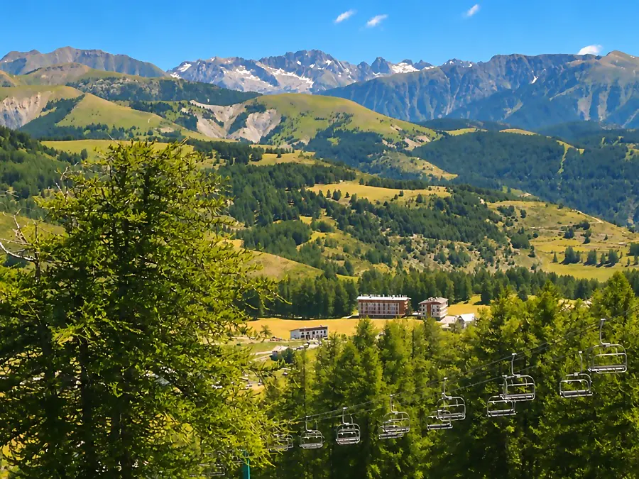 Larches, a chairlift and hotels of Valberg among the meadows, with peaks in the distance