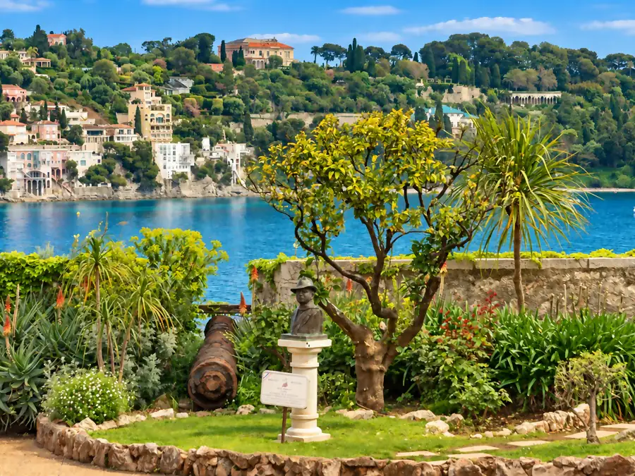 Un jardin fleuri au-dessus de la rade, un buste et un vieux canon, les villas de l’autre rive au fond