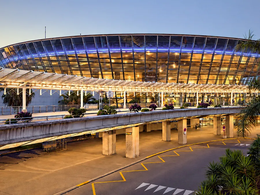 Terminal vitré de l’aéroport de Nice Côte d’Azur au crépuscule, entouré de palmiers